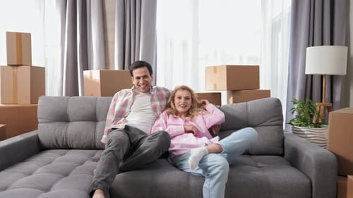 Casal feliz pula no sofá sorrindo, retrato de família, pessoas se mudando para uma nova casa
