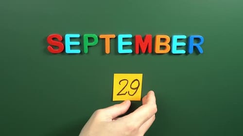 Hand sticking a sticker 29 September calendar day on school board. 29 date of September. Twenty