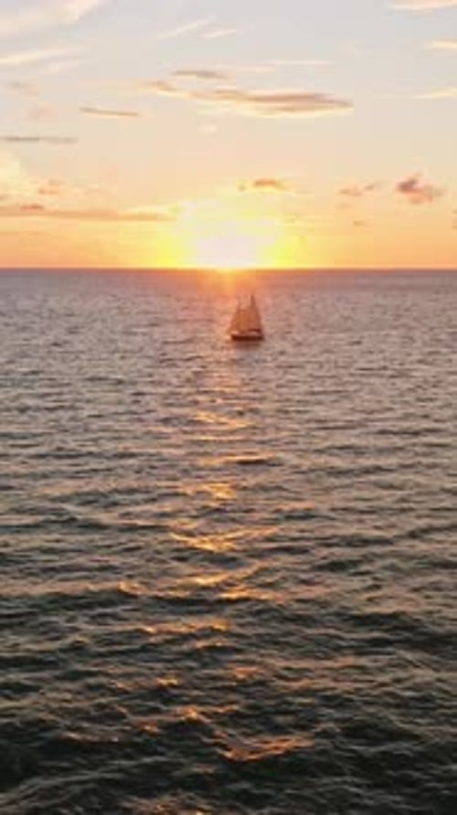 Sailboat crossing ocean at golden sunset with glowing horizon