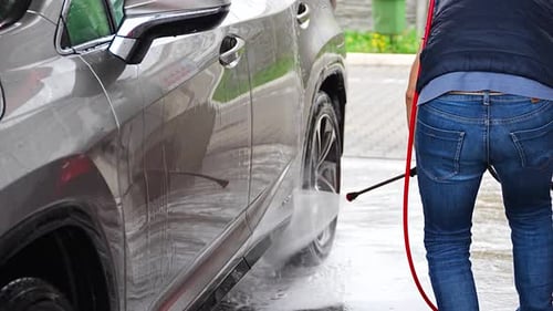 Young Man Washes His Car at a Selfservice Car Wash Using a Hose with Pressurized Water and Foam