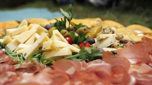 Assiette avec des produits locaux, du salami, du prosciutto, du fromage, de la roquette, des olives placées à l'extérieur sur de l'herbe, sur le côté gauche