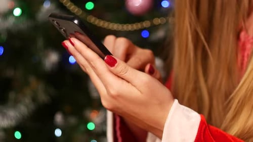 Woman Uses A Smartphone Against A Christmas Tree