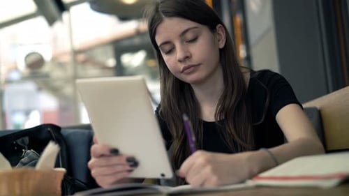 Teenage Girl with Tablet Doing Homework Sitting in Cafe Alone