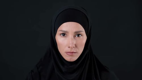 Selbstbewusste Frau im schwarzen Hijab mit ernstem Ausdruck auf dunklem Hintergrund