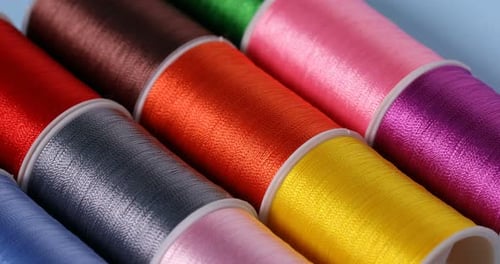 Spools of sewing threads on light blue background, closeup. Camera moving left