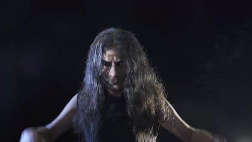 Man with Long Hair Gesturing in Stage Lighting