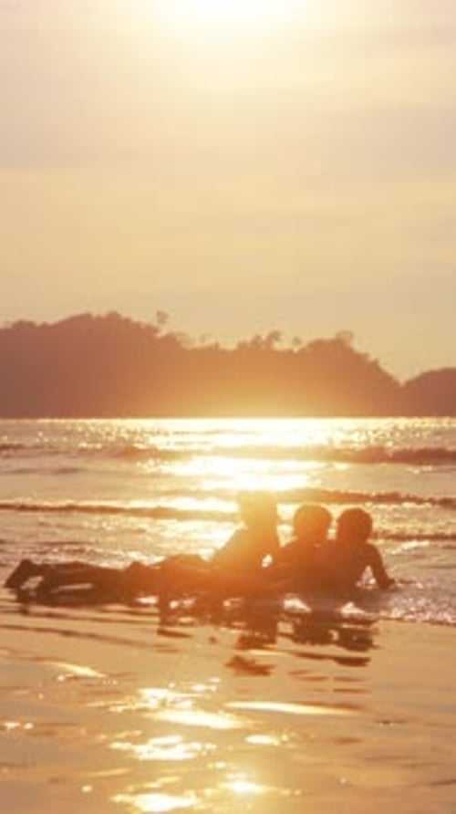 Kids Enjoying The Sunset Lying On The Sand With Glinting Waters