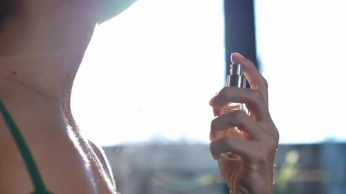 Side View Unrecognizable Woman Spraying Perfume in Slow Motion at Background of Sunny Window Indoors