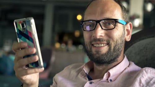 Portrait of Young, Happy Man with Smartphone Sitting in Cafe 30s