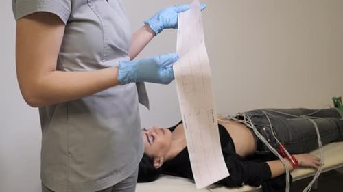 Médico cardiólogo que observa el cardiograma de una paciente, una mujer yace en segundo plano