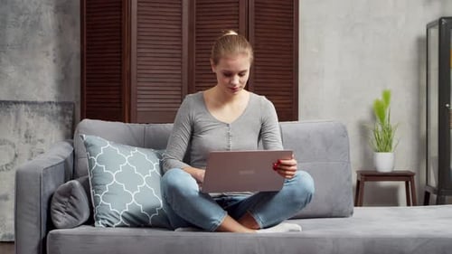 Young Woman Works Using a Laptop While Sitting on the Sofa Student Entrepreneur or Freelancer Girl