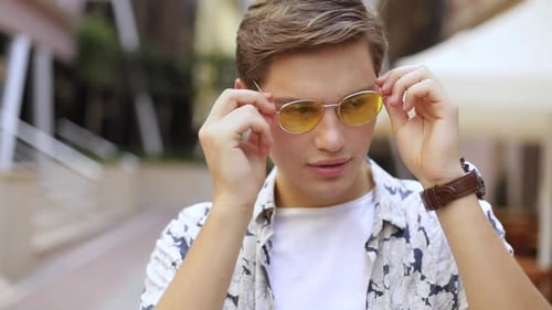 Man Puts on Yellow Tinted Sunglasses in Urban Setting