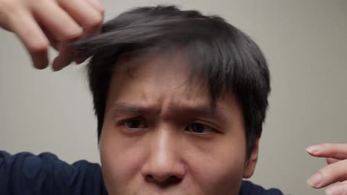 Chinese Man Fixing His Messy Hair In Front Of Mirror. - closeup shot