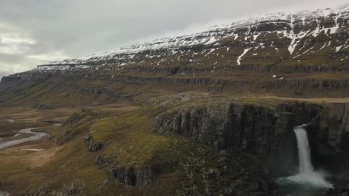 Wasserfall strömt in das üppige schneebedeckte Tal in Island