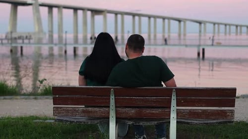 Couple Sitting on Bench near Water at Sunset