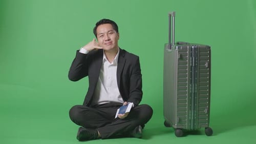 Businessman With Luggage Smiling And Making Call Me Gesture While Sitting In The Green Screen
