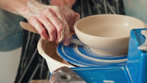 A female potter iworks on a potter's wheel, making a ceramic pot from clay in a pottery workshop.