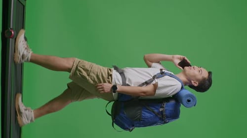 Side View Of Asian Male Hiker Talking On Smartphone While Walking On A Treadmill On Green Screen