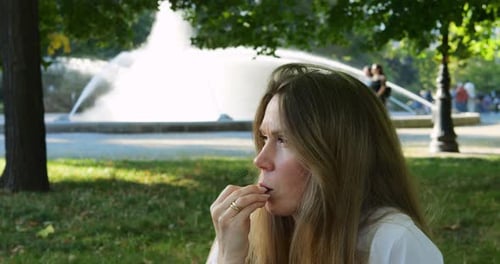 Adult Woman Finishes Sandwich Near Fountain with Quiet Joy Reflecting in Eyes