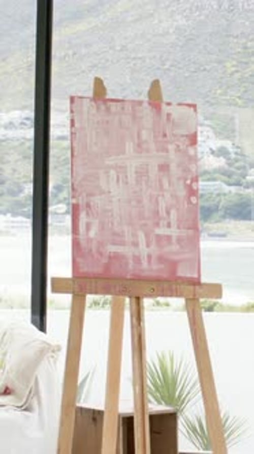 Vertical video: Starting camera framing easel holding pink canvas in studio capturing water view