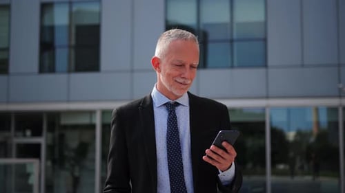 Man in Suit Using Smartphone in Front of Building