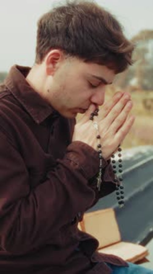 Young Man Holds Rosary with Hands Clasped in Prayer