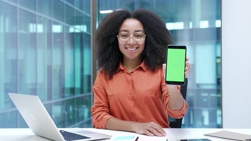 Happy african american businesswoman showing mobile phone smartphone with green screen sitting