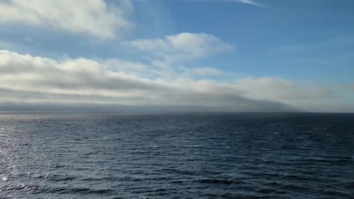 Vast Open Blue Ocean with Sunlight Sparkles on Rippling Water and Cloudy Horizon
