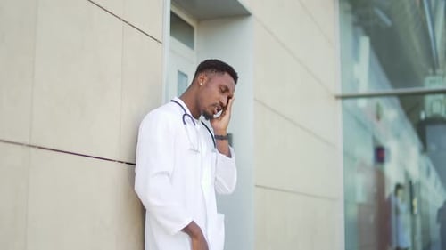 Stressful African American doctor standing outside a hospital Outdoors Tired pensive physician near