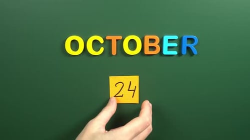 Hand sticking a sticker 24 October calendar day on school board. 24 date of October. Twenty fourth