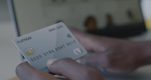 Closeup of Male Hand Holding Credit Card and Typing with Laptop Computer at Desk