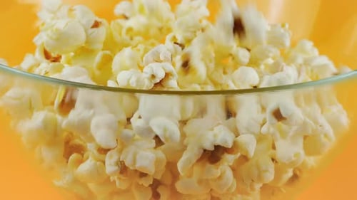 Popcorn grains falling into glass transparent bowl isolated on peach background. Slow motion.