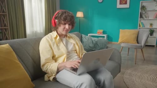 Young Adult Using Laptop on Couch with Headphones