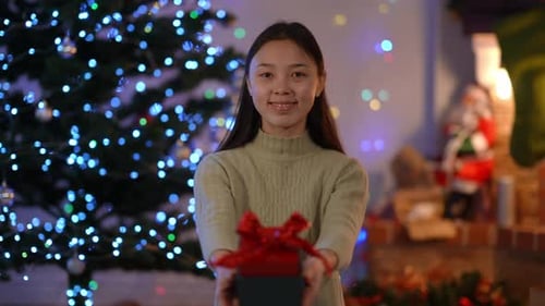 Front View Portrait of Slim Charming Asian Woman Stretching Gift Box Looking at Camera Sitting at