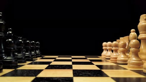 Dolly shot forward along chess pieces standing on either side of a chessboard against a black backgr