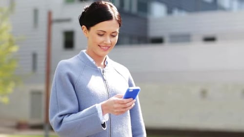 Smiling businesswoman texting on smartphone in urban city center outdoors