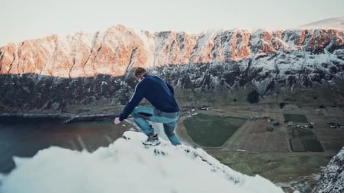 Slow motion shot of a young man walking on a very thin mountain ledge, beautiful sun shining on moun