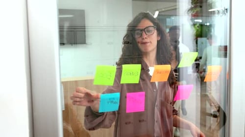Businesswomen Planning and Brainstorming Using Sticky Notes on Glass Wall