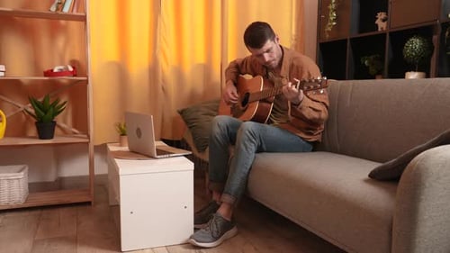Man Plays Guitar While Using Laptop at Home
