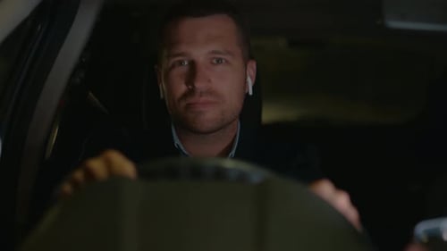 Man Holding the Steering Wheel with Two Hands and Listening to Music in Wireless Headphones in the