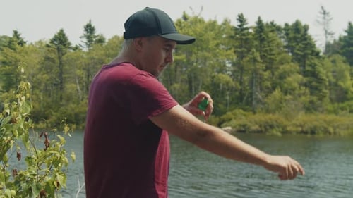 Man Using Mosquito Repellent Spray By the Lake in Sunshine