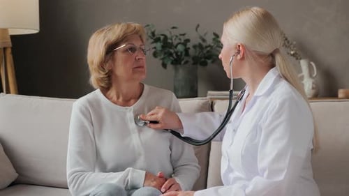 A Young Female Doctor Listens to the Patient's Heart Using a Stethoscope