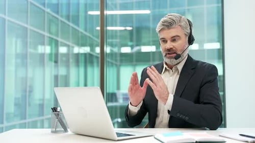 Confident businessman in a headset talking on a video call conference using laptop in office.