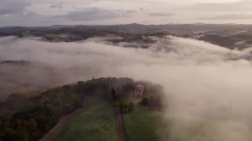Aerial view of foggy sunrise over villa and cypress trees, Italy.