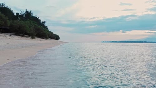 Low flying drone shot of a tropical sandy beach with turquoise water before sunrise, early morning.