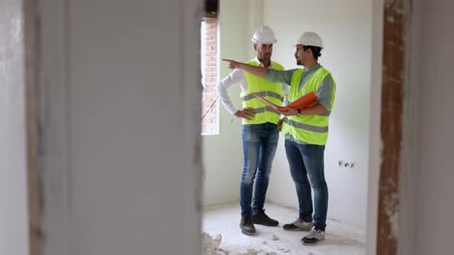 Two Construction Workers Reviewing Building Plans Indoors