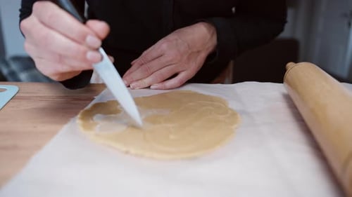 A woman is cutting out a gingerbread cookie from the dough in the shape of a person.