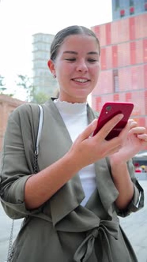 Young Woman Happily Engaging with Her Smartphone While Enjoying a Sunny Day Outdoors in the City