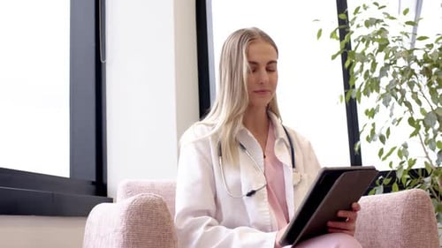 Frau im Laborkittel mit Stethoskop bereitet sich auf eine klinische Beratung vor, Notizen auf der Tablette mit Blick nach links