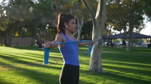 A slim young woman working out in a park with fitness resistance bands to train and strengthen her t
